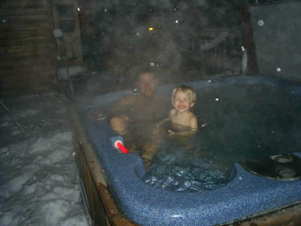 Happy boy with the father in a hot tub in winter at night